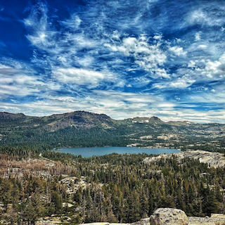 Image of a mountain with white clouds and a lake surrounded by many trees and granite rocks